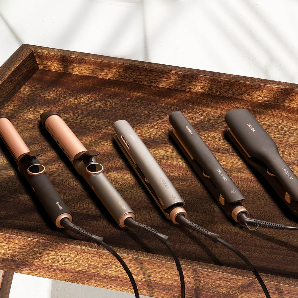 Cinco planchas y rizadores de pelo en varios colores sobre una superficie de madera.