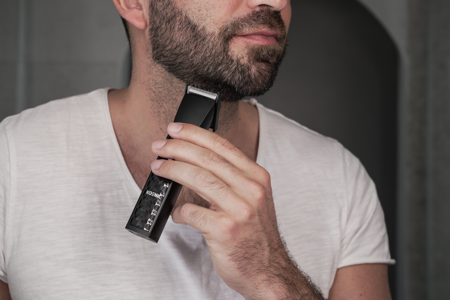 Hombre se recorta la barba con recortadora negra. Camiseta blanca.