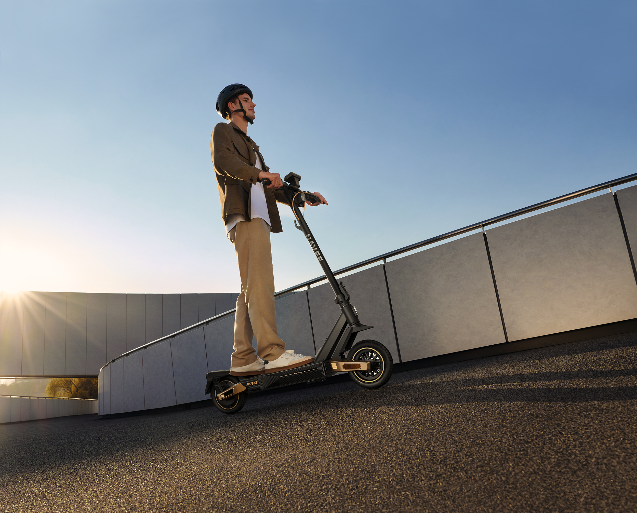 Mann mit Helm fährt E-Scooter auf asphaltierter Straße vor modernem Gebäude.