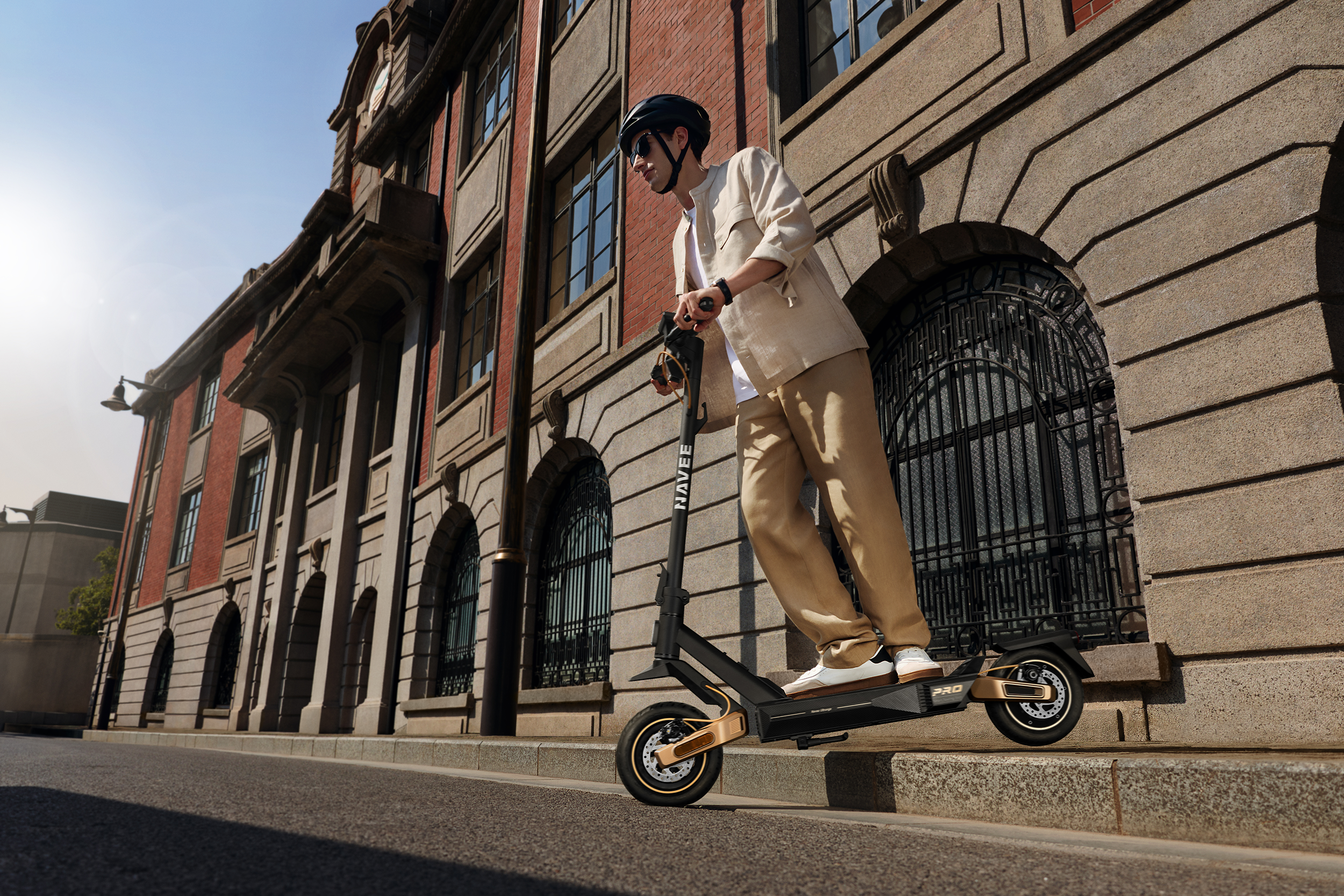 Mann mit Helm fährt E-Scooter vor Backsteingebäude mit Steinfassade.