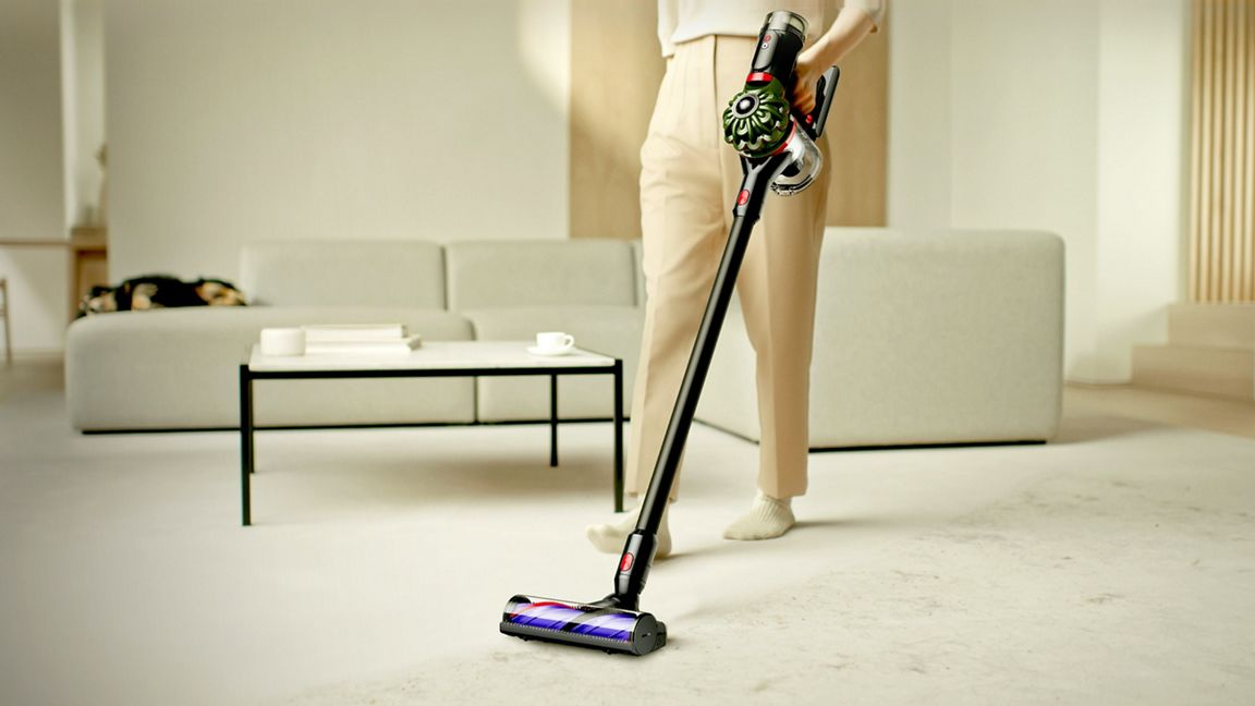 Una persona aspira un tappeto chiaro con un aspirapolvere nero portatile.