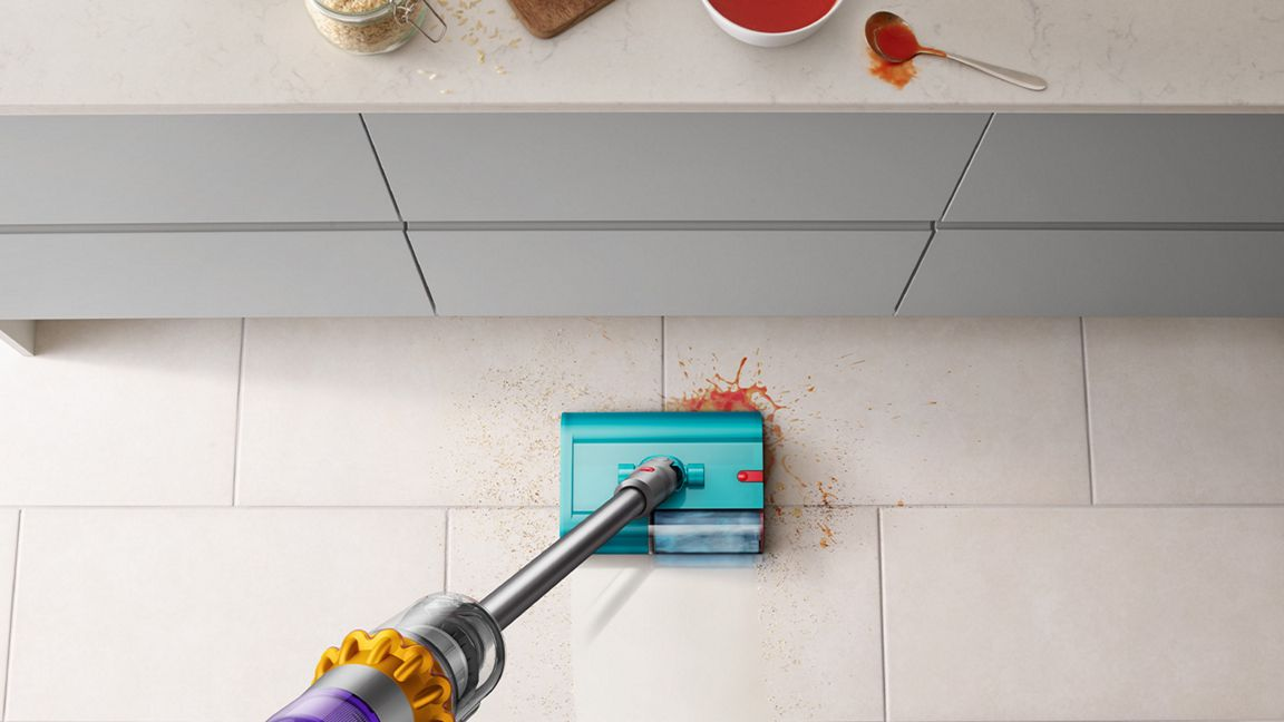 Ein blauer Dyson-Mopp reinigt rote Flecken auf einem hellen Fliesenboden.