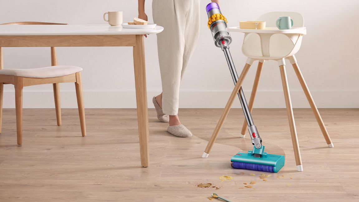 Ein Staubsauger reinigt einen verschmutzten Holzboden neben einem Hochstuhl und Tisch.