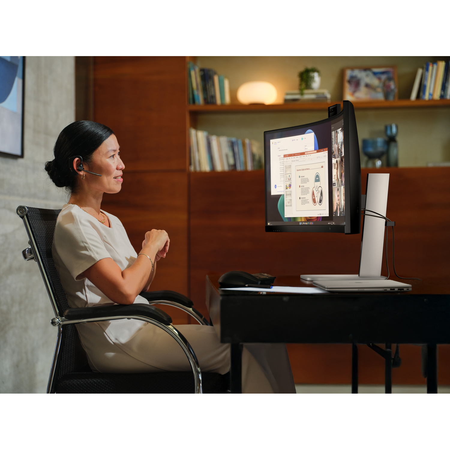 A woman sits at a desk, looking at a computer screen.