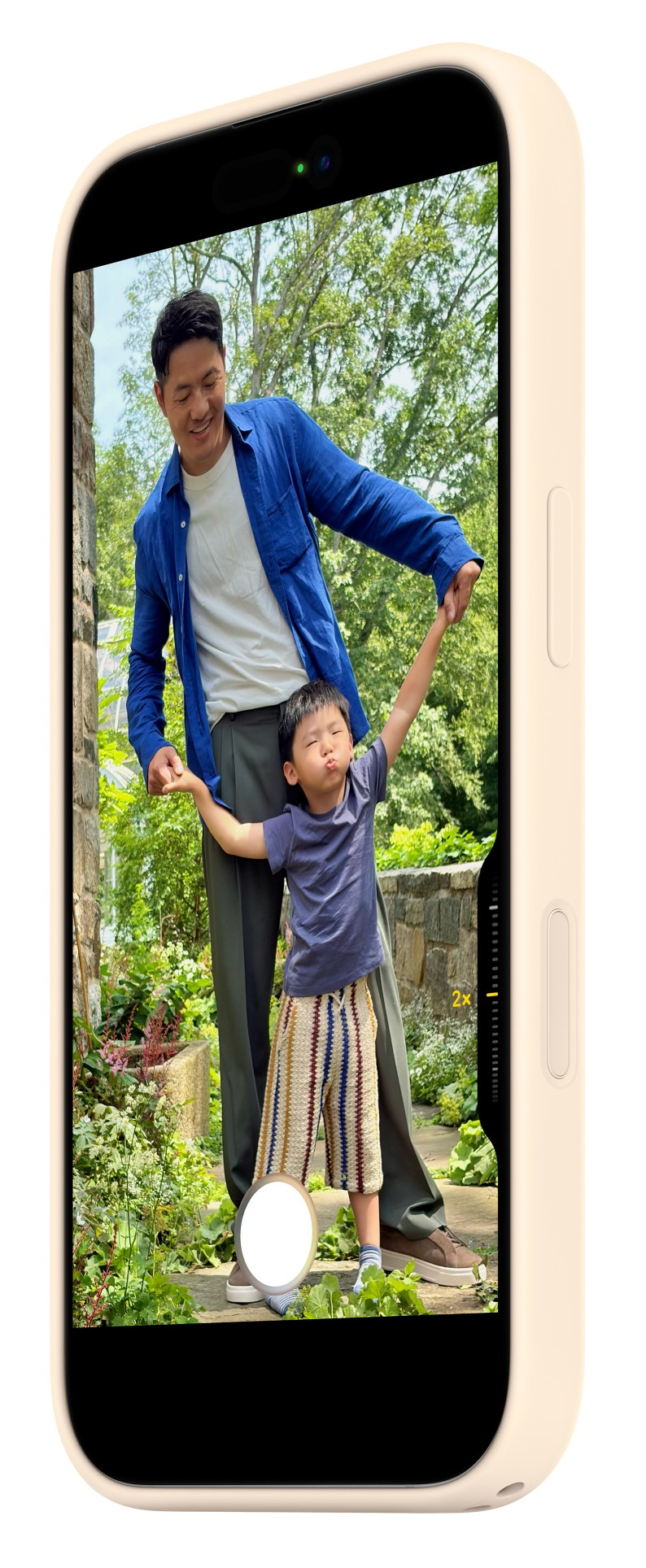 Mężczyzna trzyma dziecko za rękę na zewnątrz, z drzewami i kamiennymi murami.