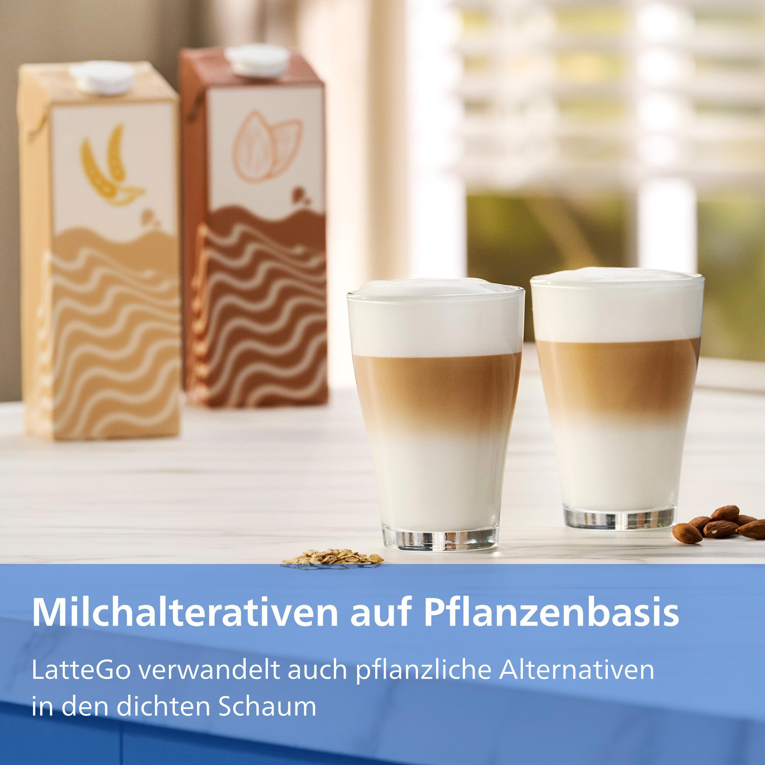 Zwei Latte Macchiato Gläser neben Pflanzenmilchkartons und Mandeln.