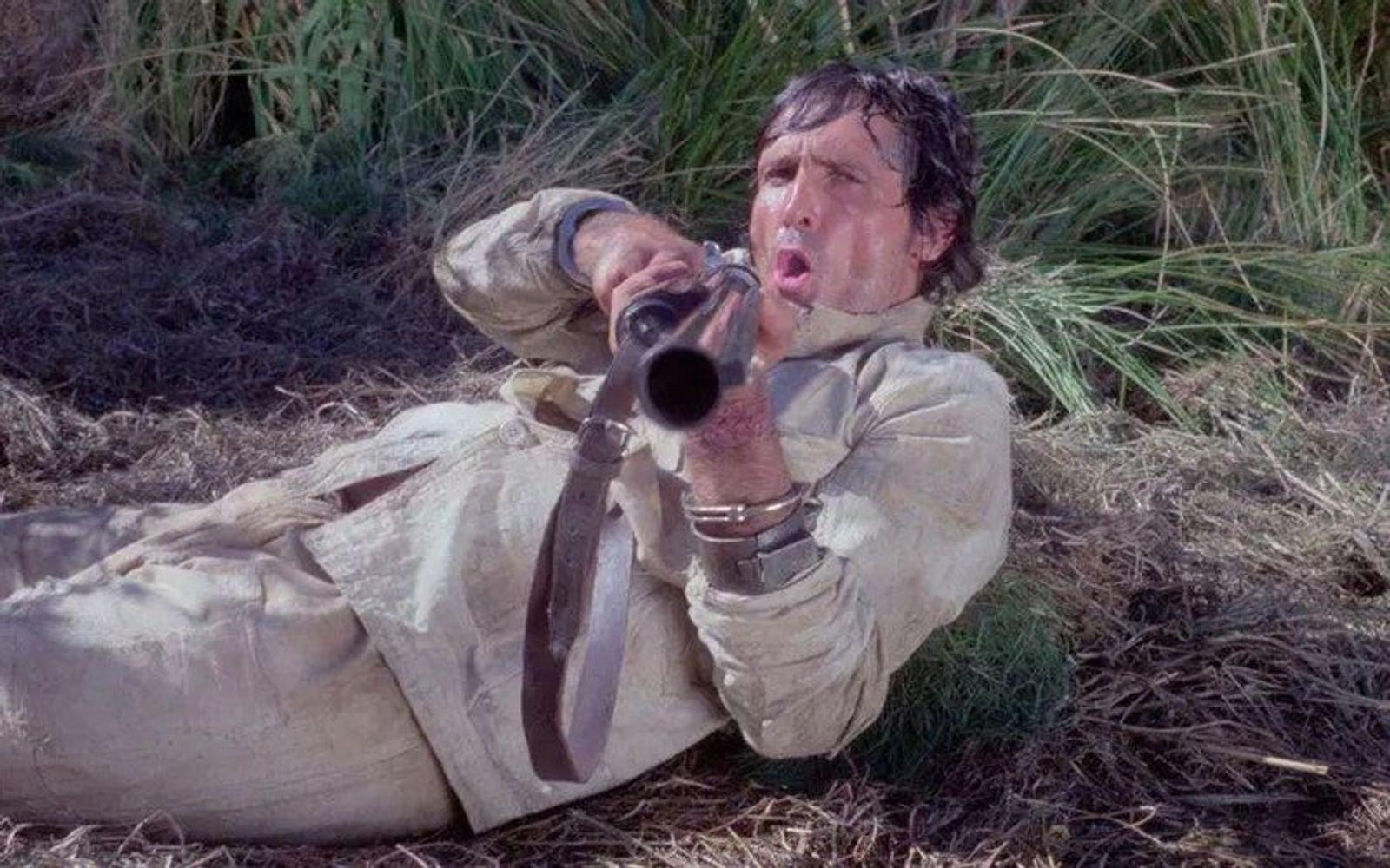 Mann liegt im Gras und zielt mit Gewehr.