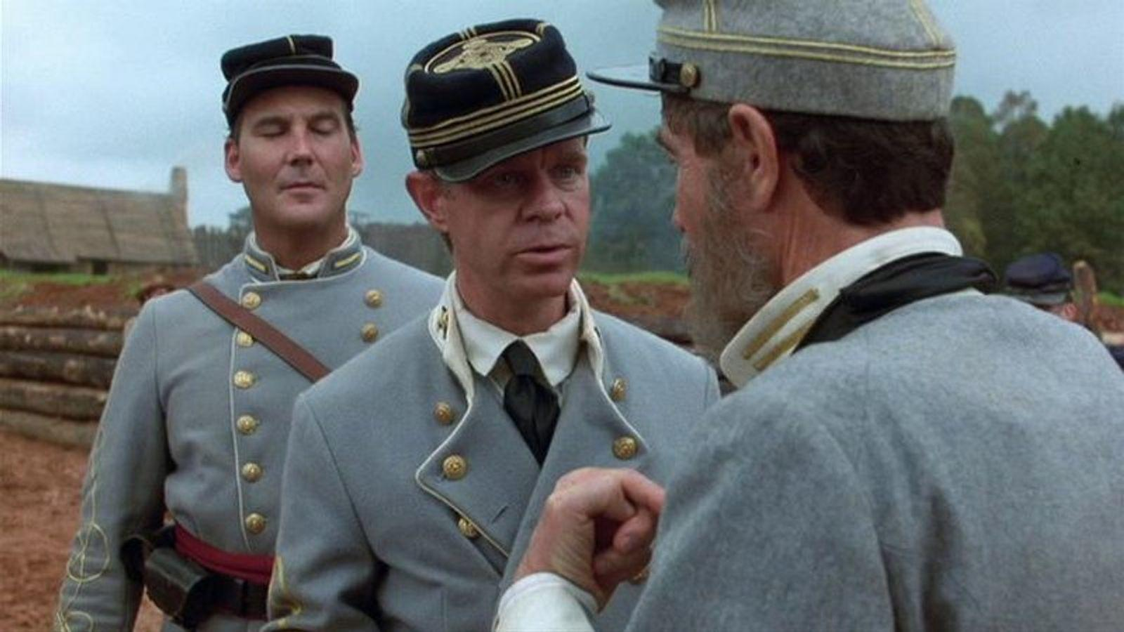 Drei Männer in Uniformen des Bürgerkriegs stehen im Freien. Im Vordergrund sprechen zwei Männer.
