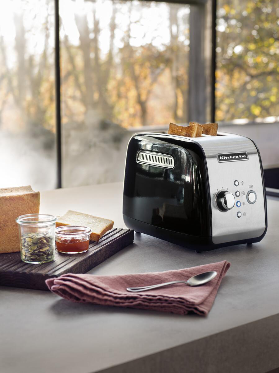 Ein schwarzer KitchenAid-Toaster mit Toast, Brot, Marmelade und Samen auf einer Arbeitsplatte.