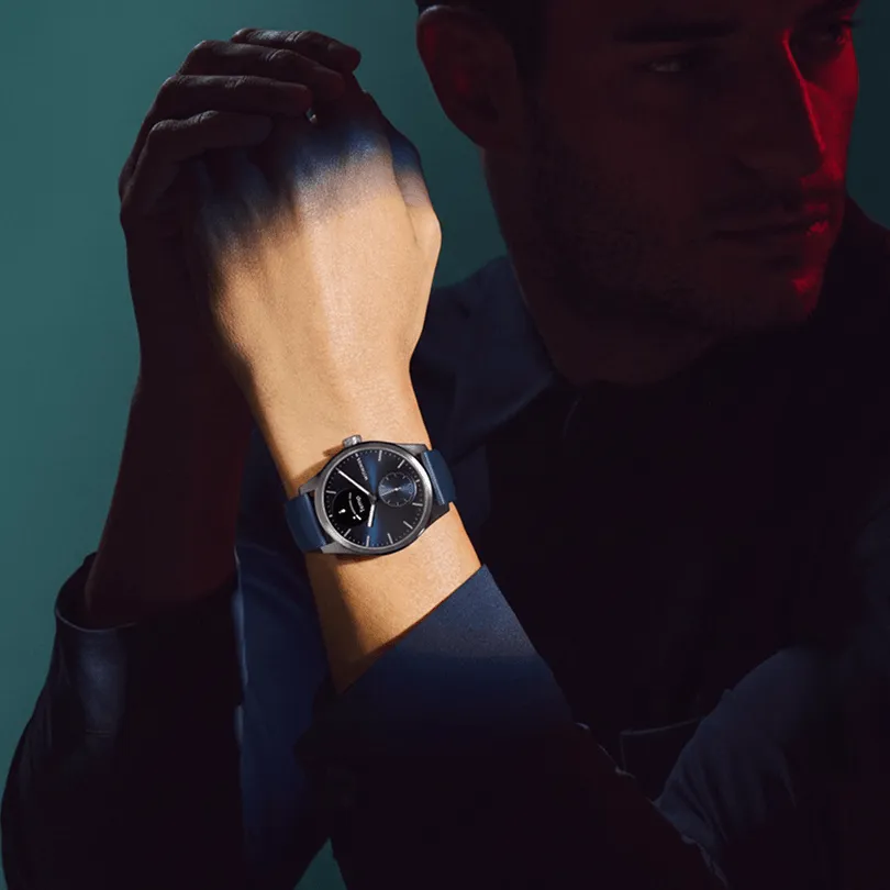 Homme en chemise sombre porte une montre à cadran bleu et bracelet bleu.