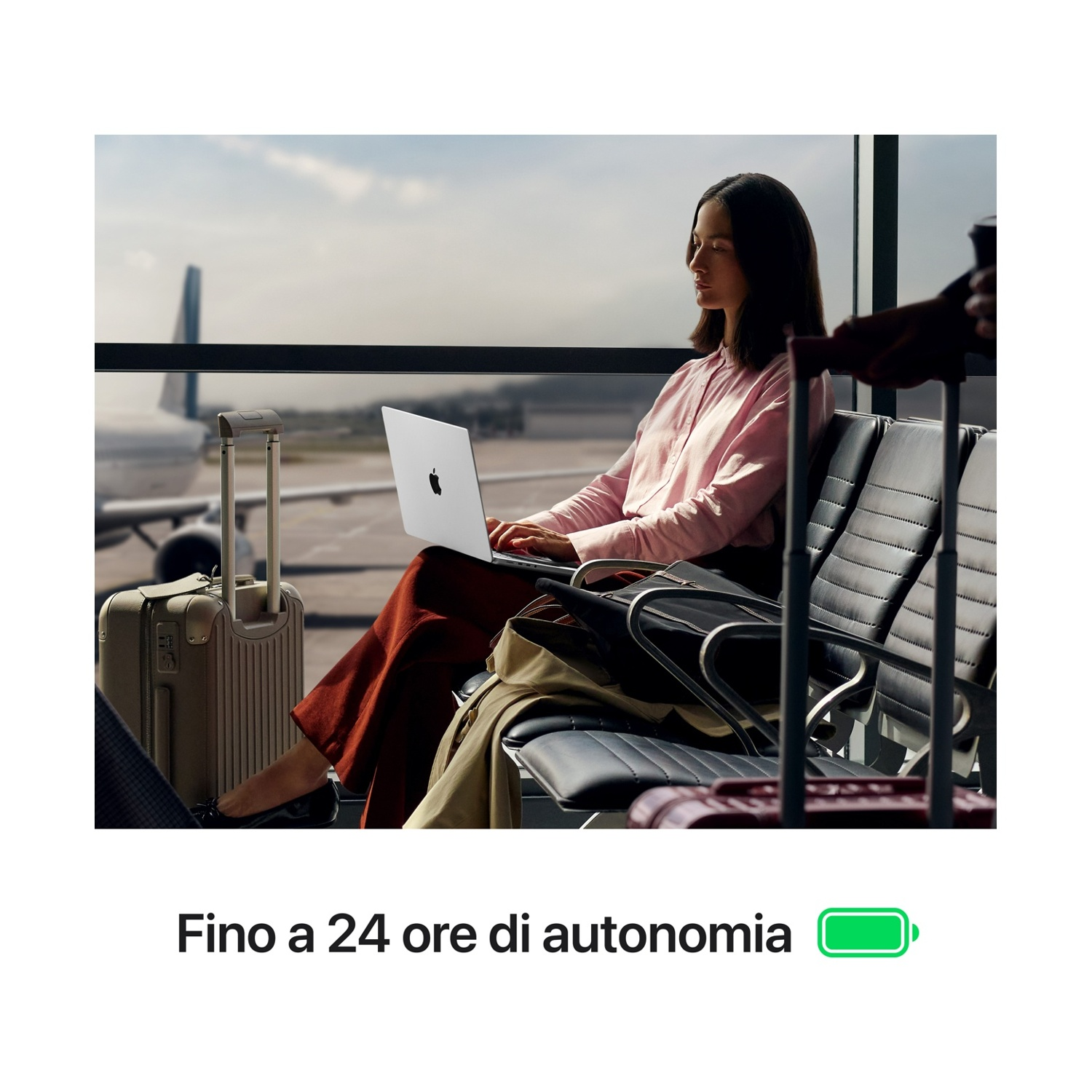 Donna lavora al laptop in aeroporto con bagagli accanto.