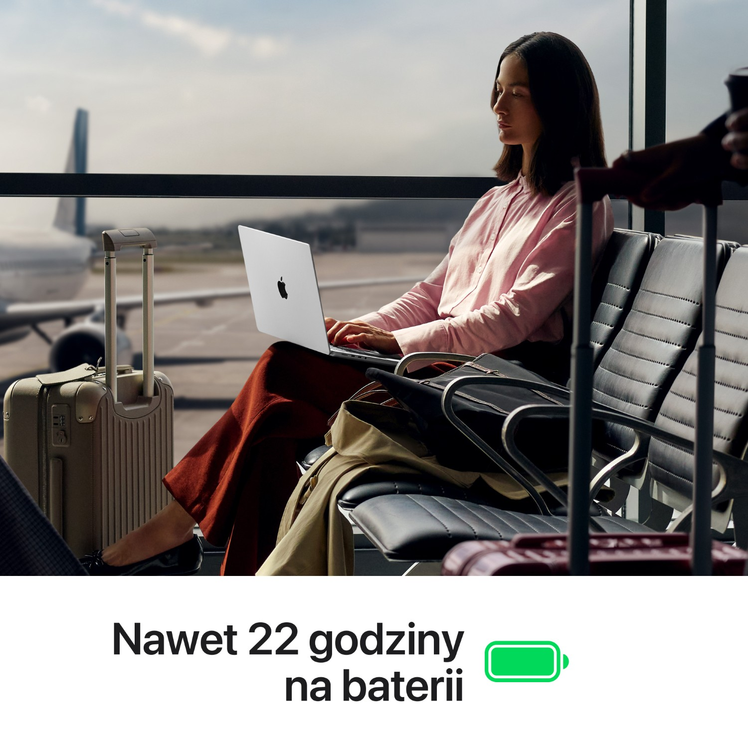 Kobieta siedzi w poczekalni lotniskowej, korzystając z laptopa, obok bagaż.