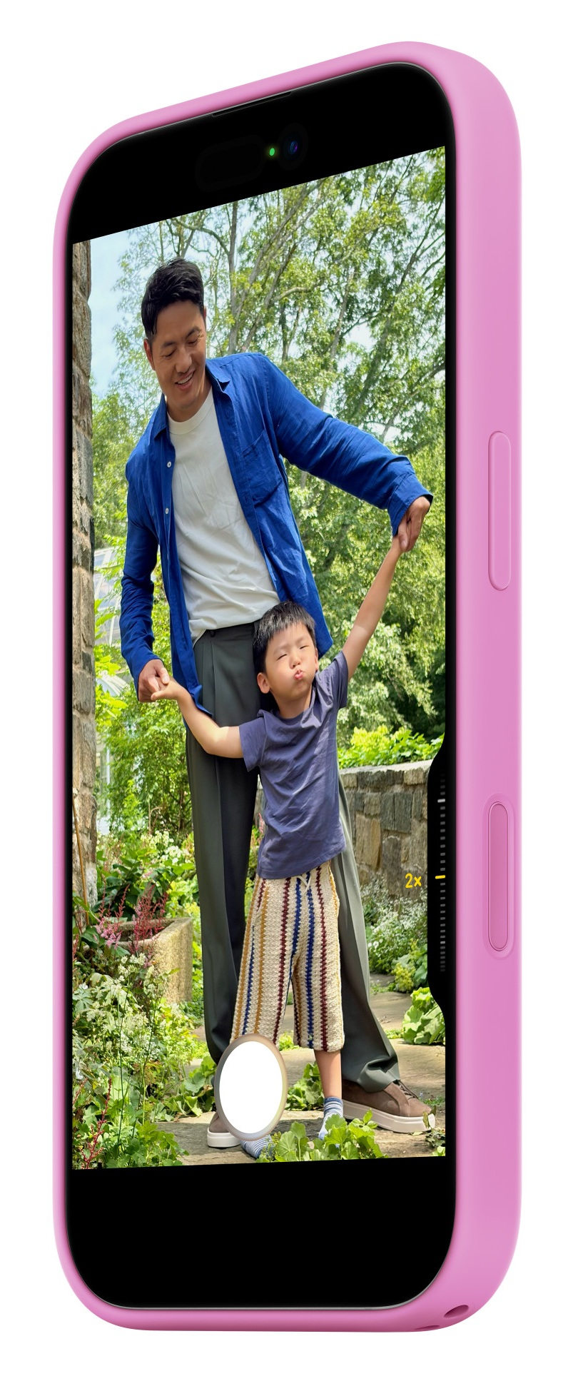 Mężczyzna i dziecko trzymają się za ręce na zewnątrz, z drzewami i kamiennym murem.