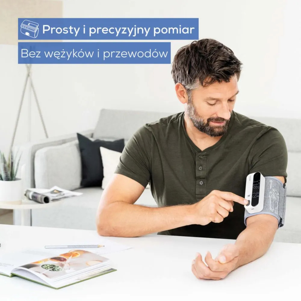 Mężczyzna mierzy ciśnienie krwi cyfrowym urządzeniem na ramieniu, siedząc.