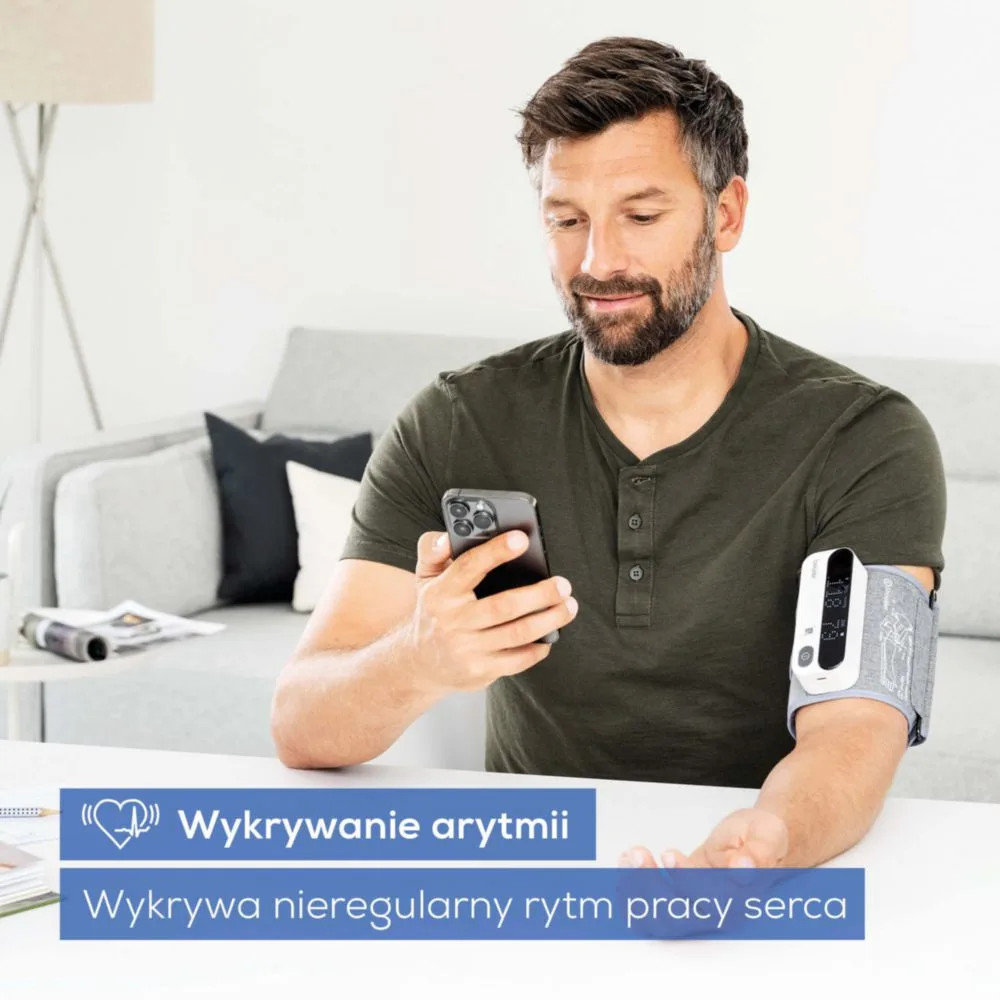Mężczyzna z ciśnieniomierzem na ramieniu i telefonem w dłoni. Wnętrze.