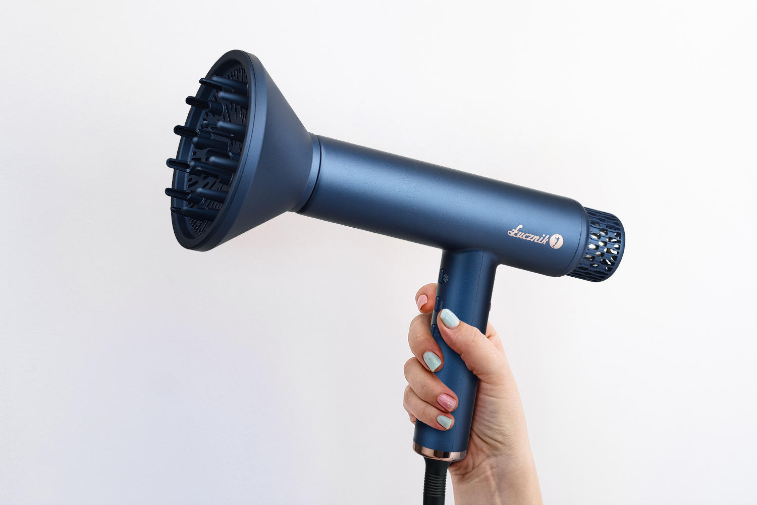 Ręka trzyma ciemnoniebieską suszarkę do włosów z dyfuzorem na białym tle.