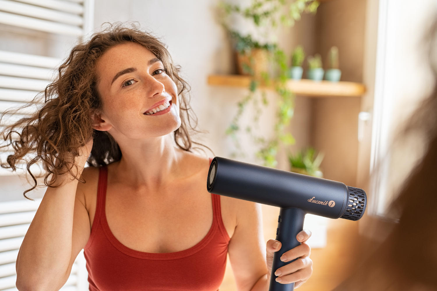 Kobieta z kręconymi włosami suszy włosy czarną suszarką.