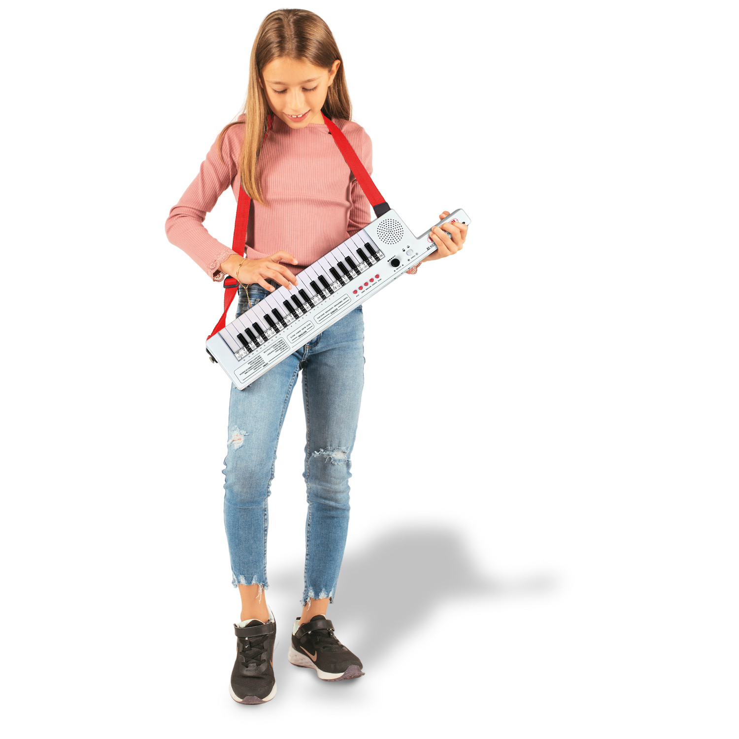 Una bambina con maglione rosa e jeans suona una tastiera bianca con tracolla rossa.