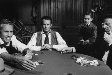 Vier Männer spielen Poker an einem Tisch mit Chips und Karten.