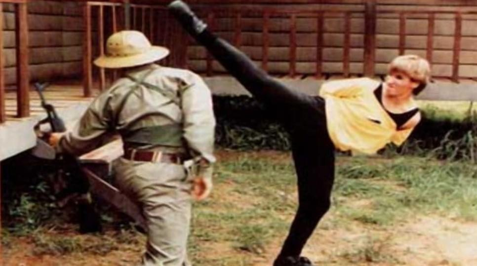 Eine Frau in Gelb tritt mit dem Bein nach oben, ein Mann mit Hut und Gewehr steht.