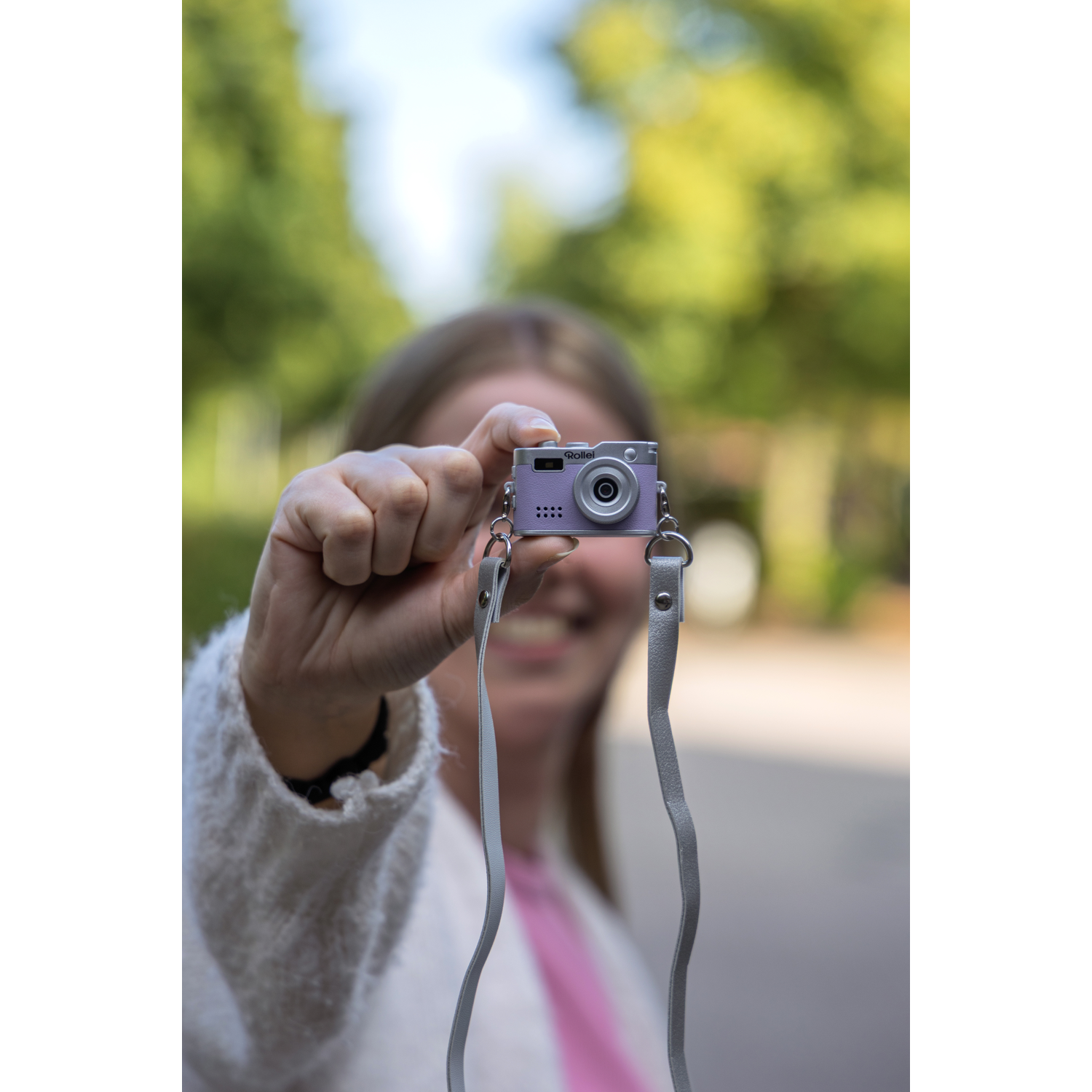 Een persoon houdt een kleine paarse camera vast voor een wazige groene achtergrond.