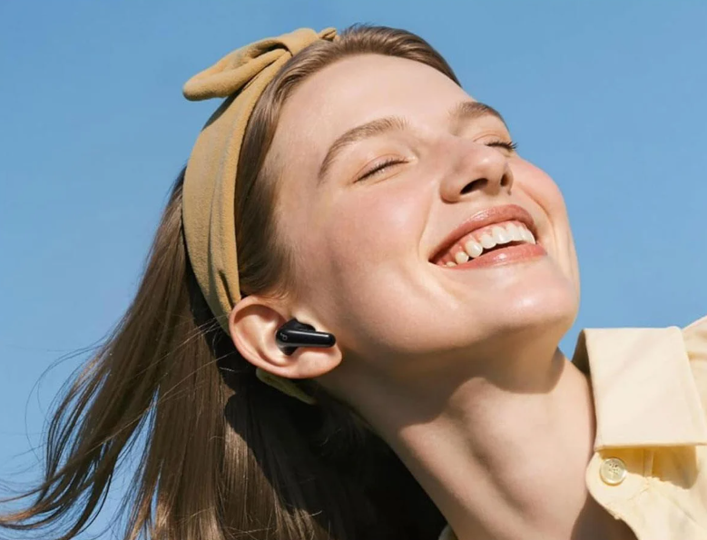 Kobieta z opaską na głowie śmieje się na tle niebieskiego nieba. Nosi słuchawkę.