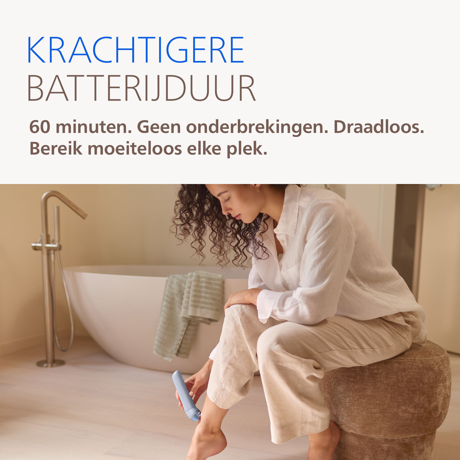 A woman sits on a stool, using a device on her leg in a bathroom.