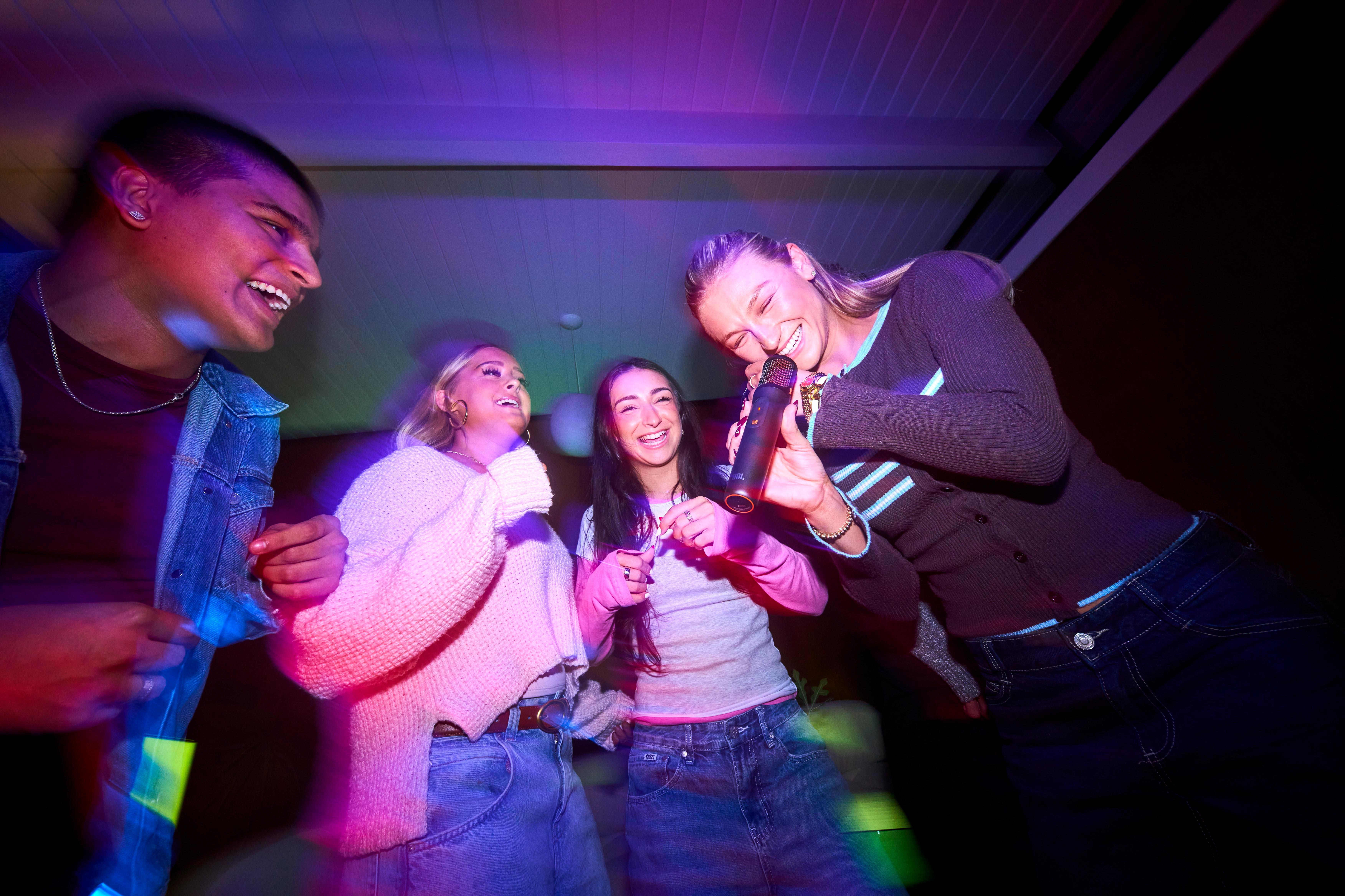 Vier Freunde singen und lachen bei Nacht mit bunten Lichtern.