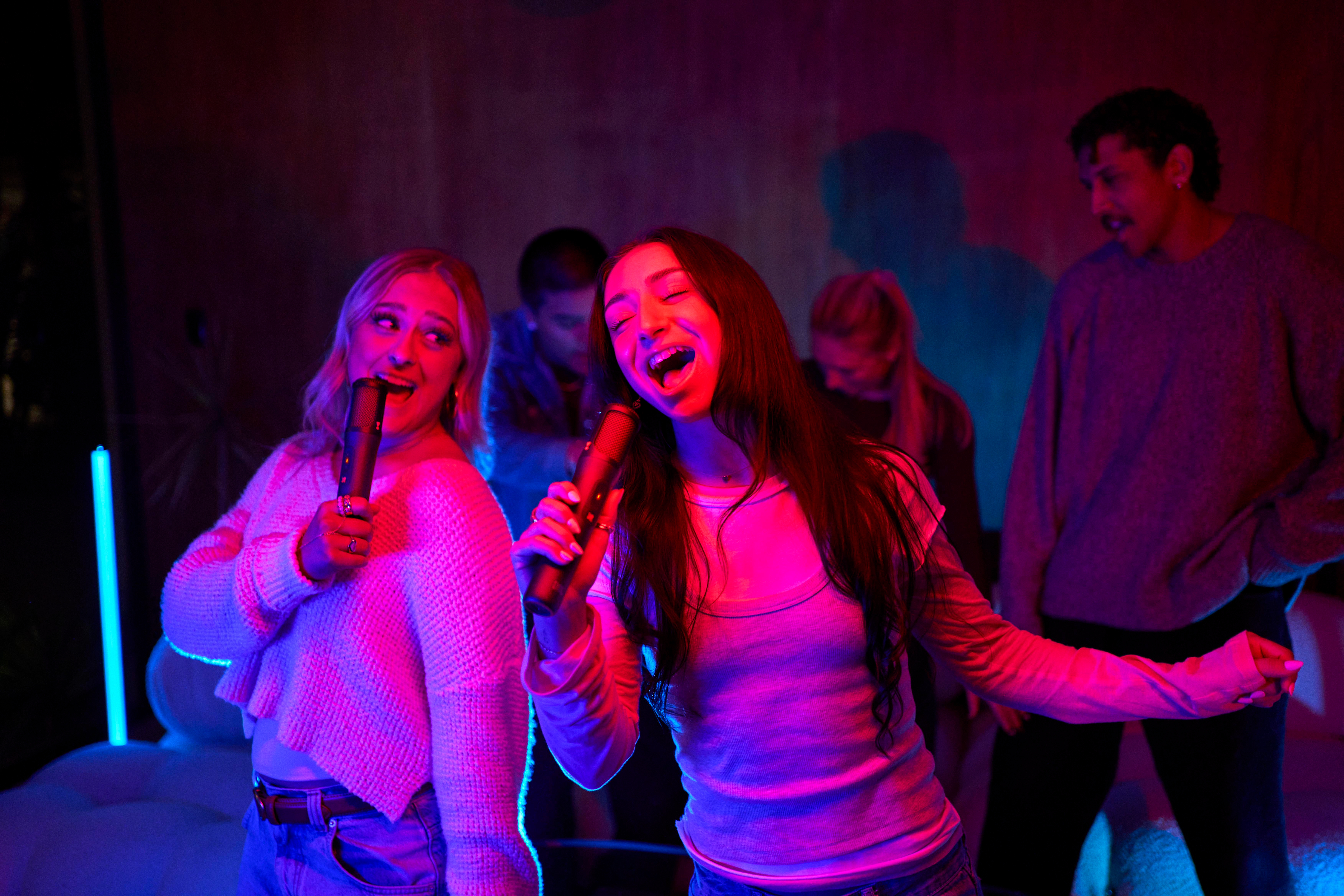 Mehrere Personen singen in einem Raum mit rotem und blauem Licht.