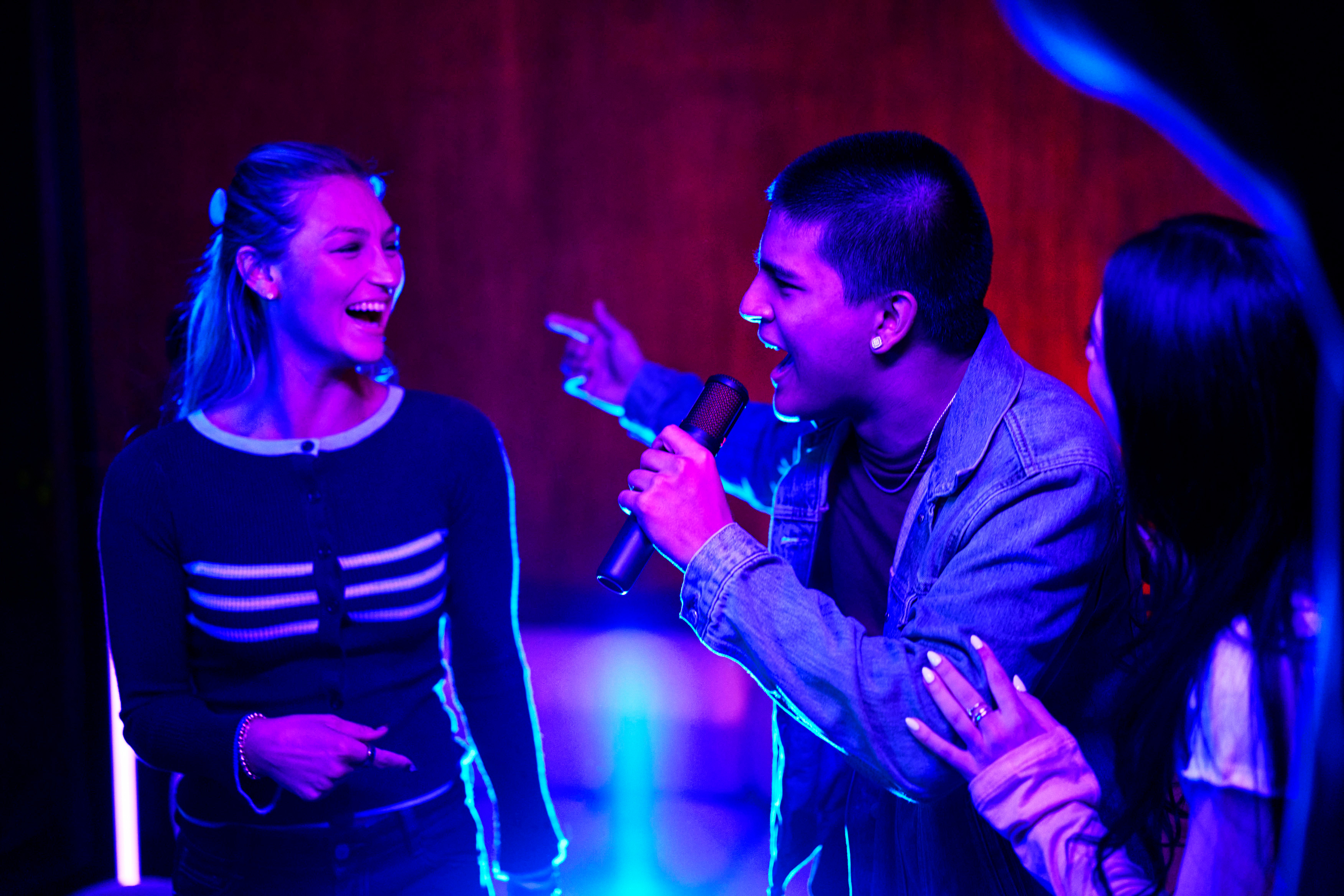 Junge Leute singen mit Mikrofonen bei Neonlicht.