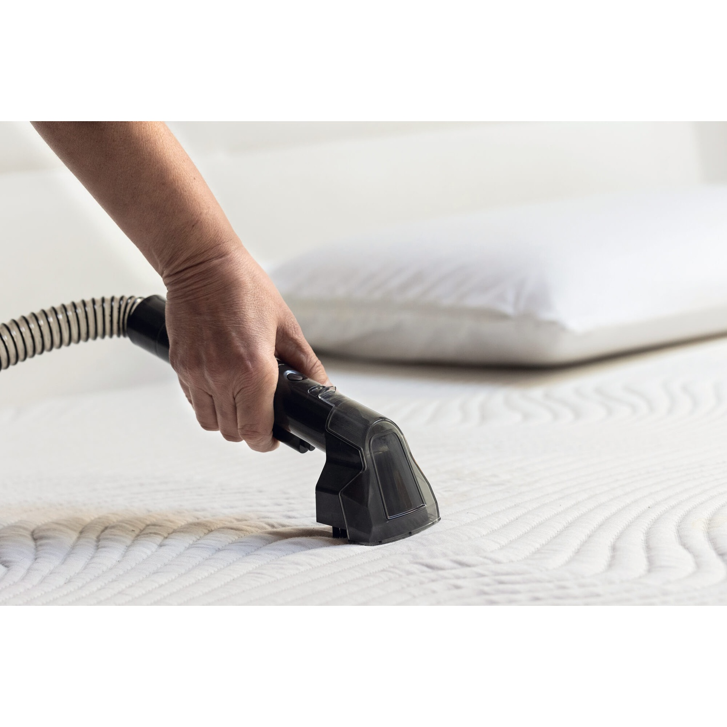 Una mano tiene un pulitore per tappezzeria nero su un materasso bianco.