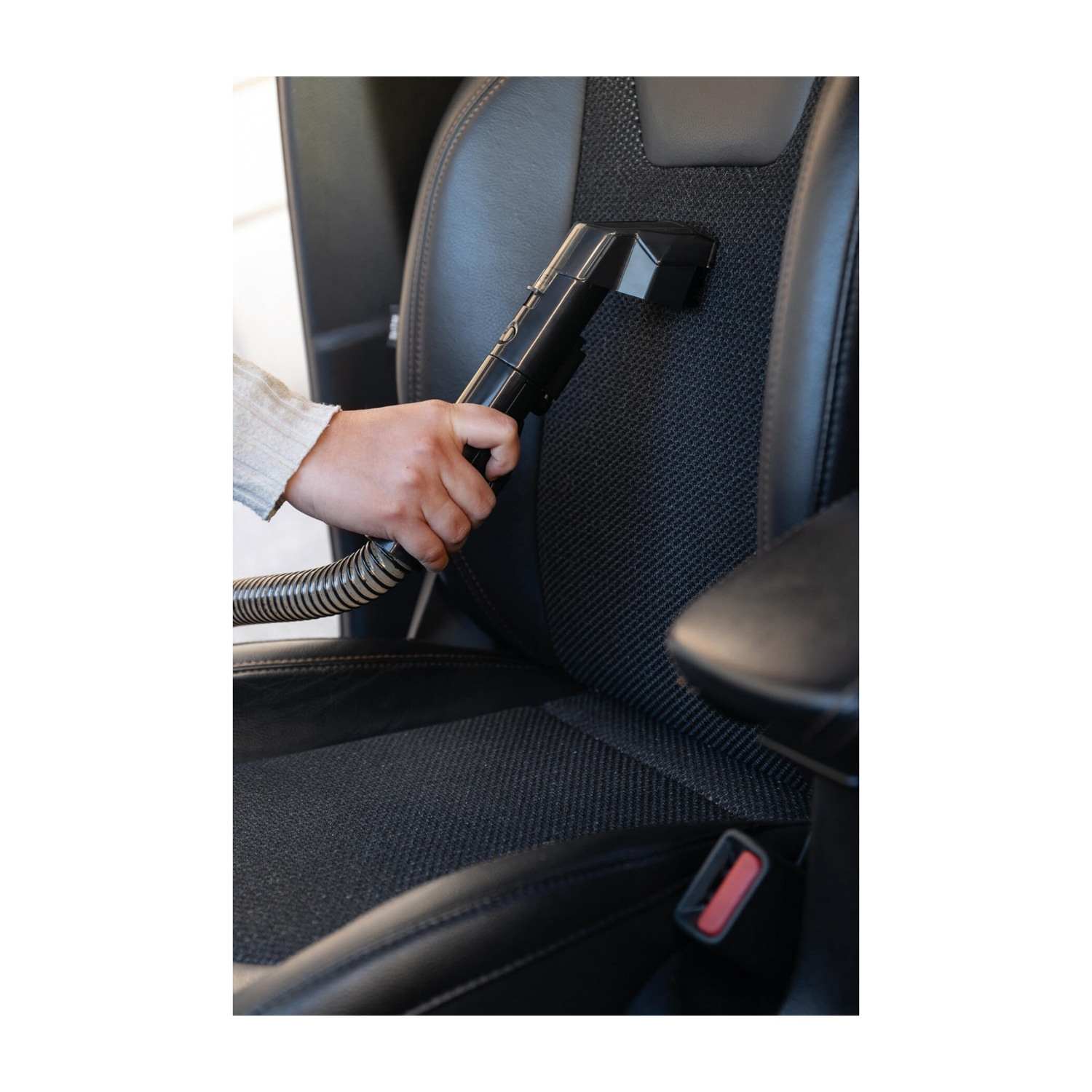 Una mano usa un aspirapolvere su un sedile dell'auto.