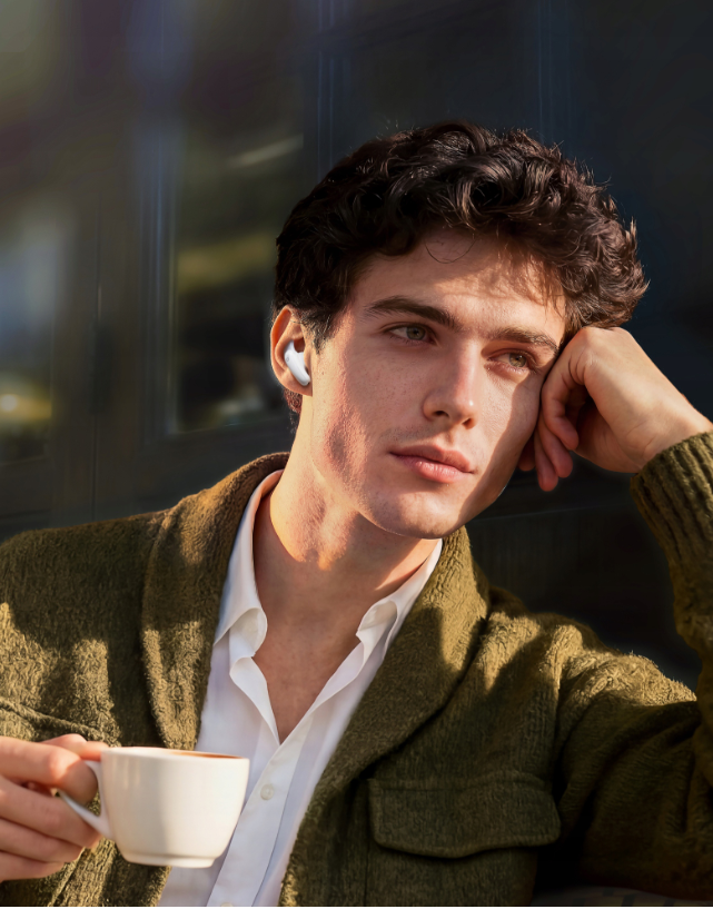 Mężczyzna w słuchawkach trzyma filiżankę kawy, zamyślony patrzy na bok.