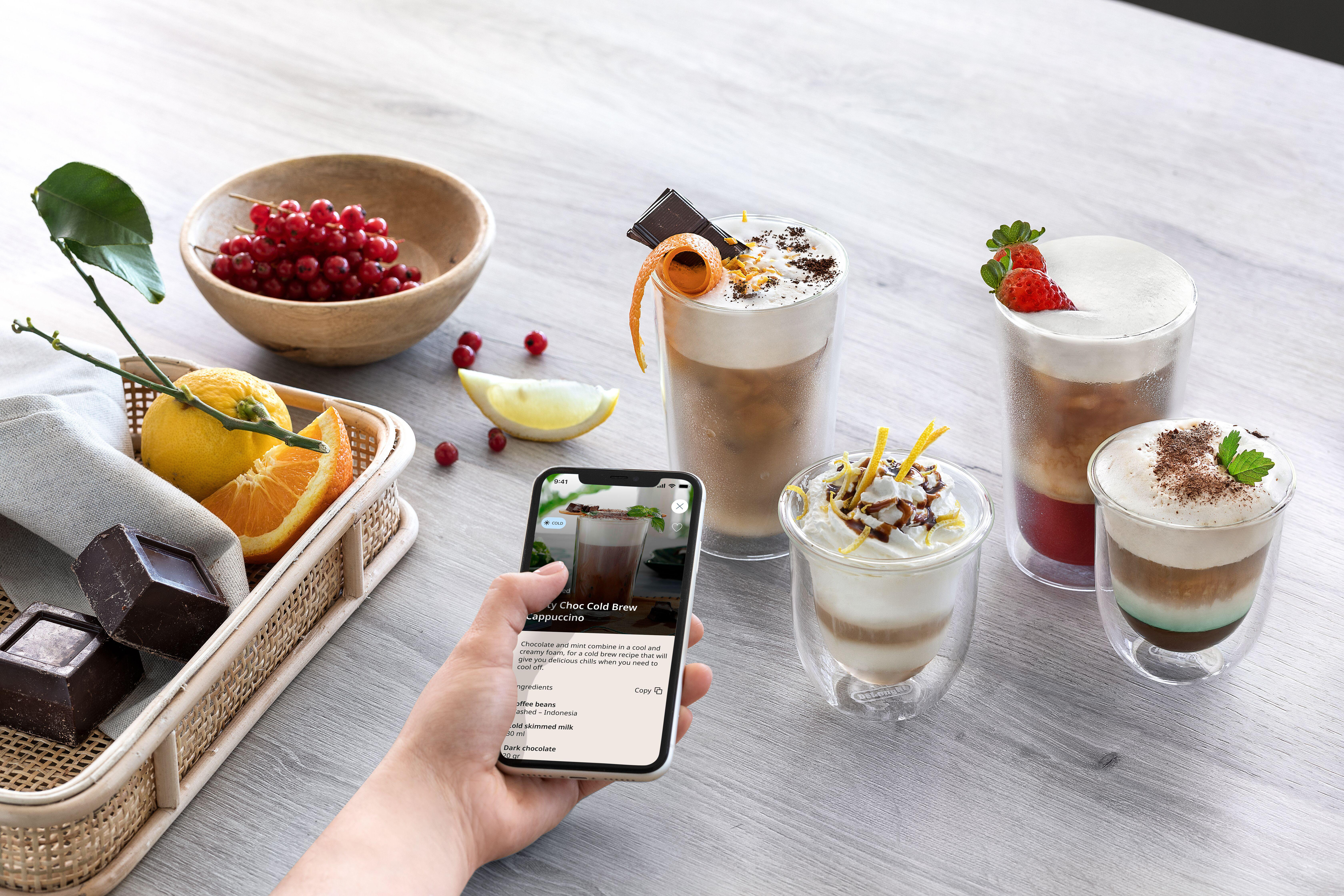 Eine Hand hält ein Handy mit einem Rezept. Mehrere Getränke sind zu sehen.