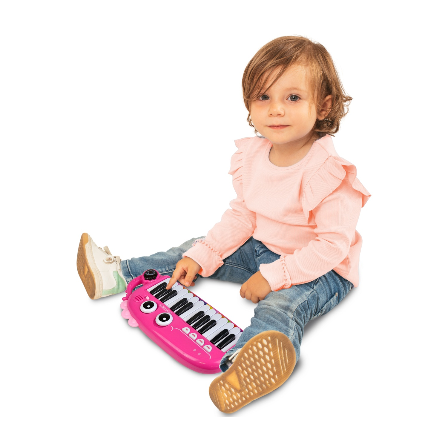Una bambina seduta per terra gioca con una tastiera giocattolo rosa.