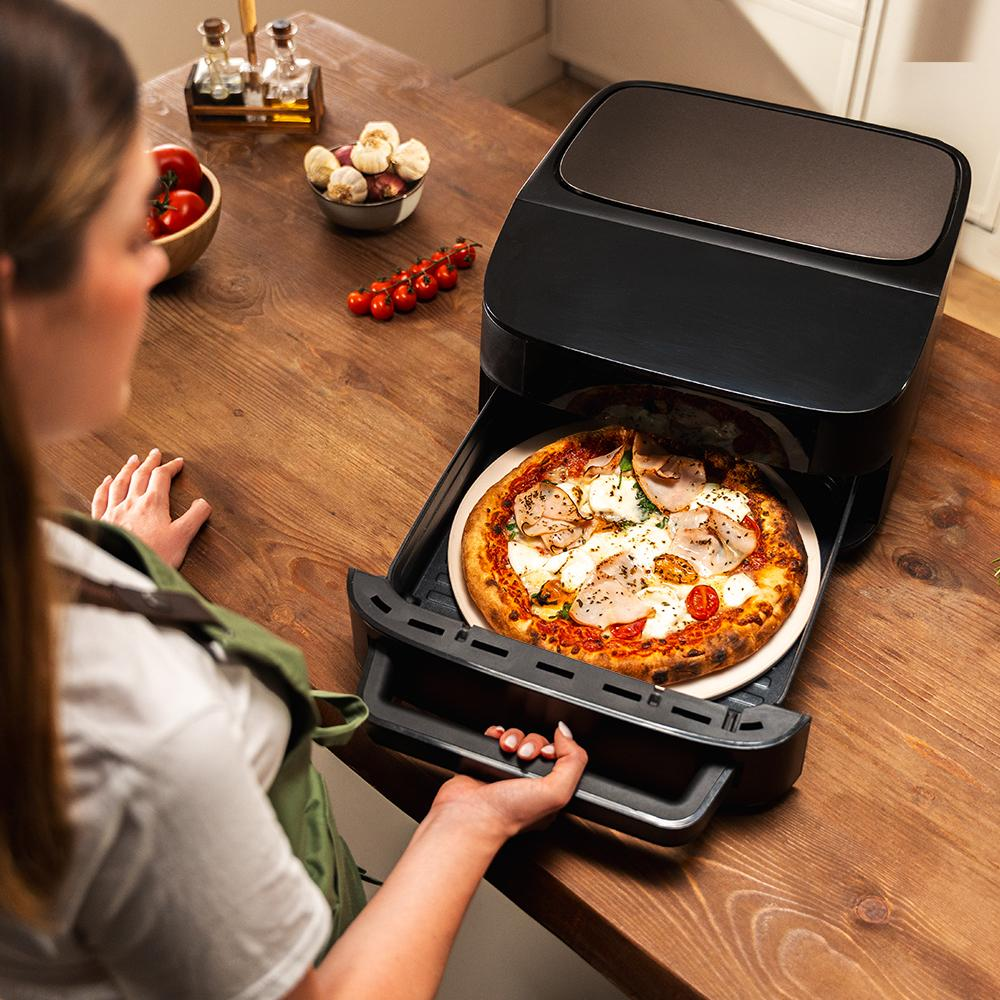 Una mujer saca una pizza cocinada de un horno freidora de aire negro.