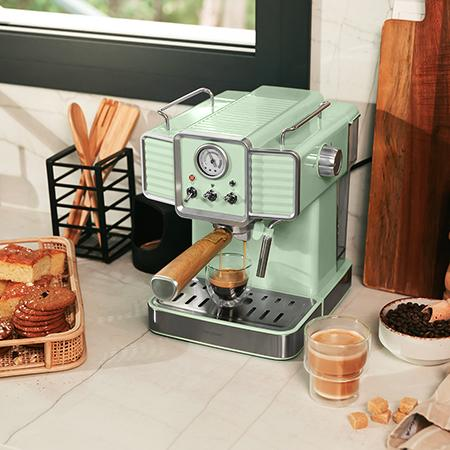 Una máquina de espresso verde menta prepara café en un vaso, con pasteles y granos de café cerca.