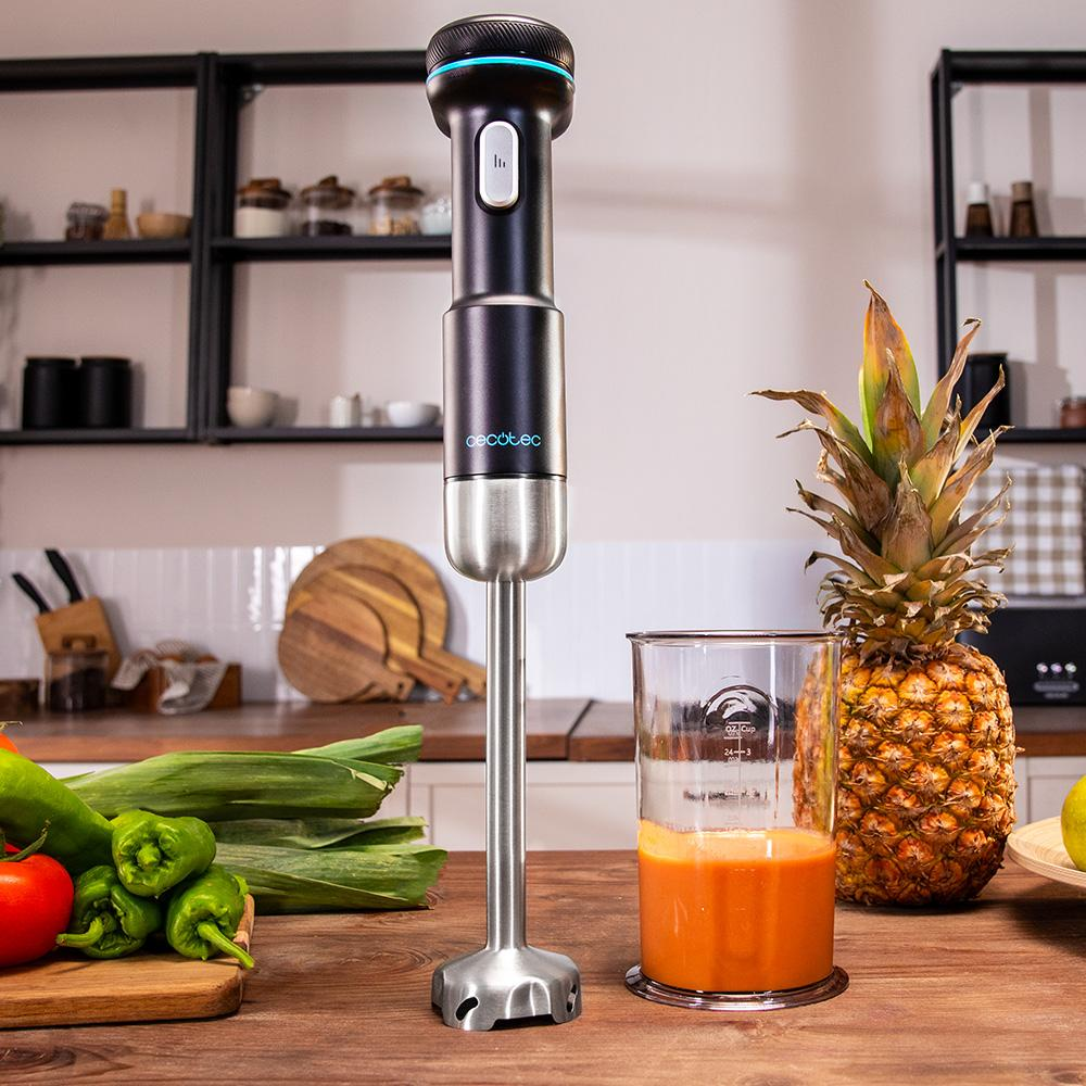 Una batidora de mano junto a un vaso de jugo y una piña en una cocina.