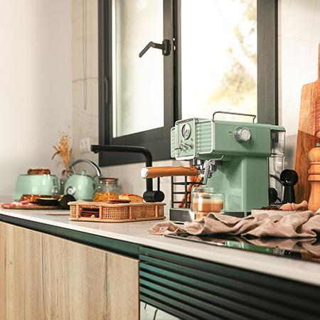 Cocina verde: Cafetera, tostadora, tetera, cesta de pan, ventana.
