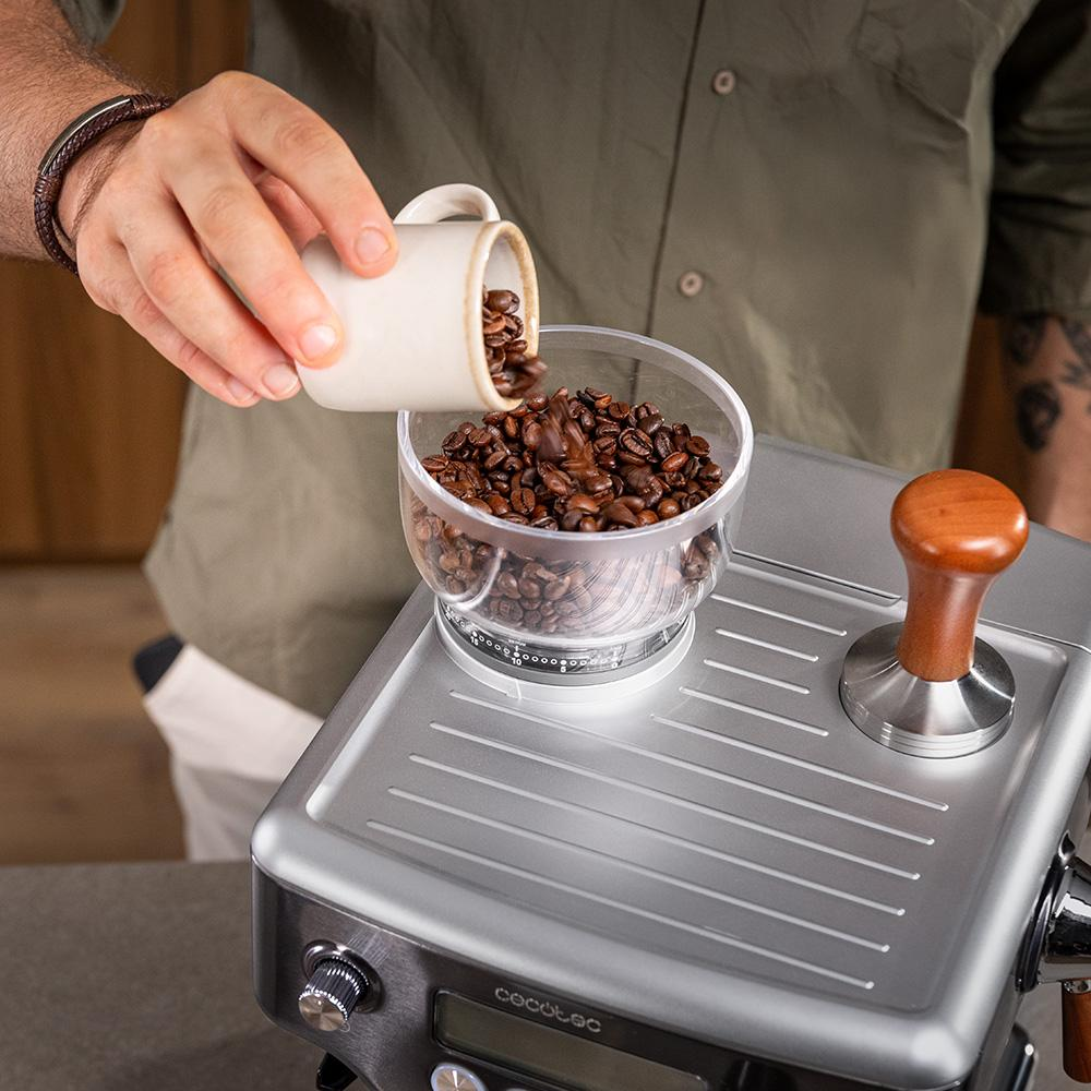 Los granos de café se vierten de una taza a un recipiente en una máquina de espresso.