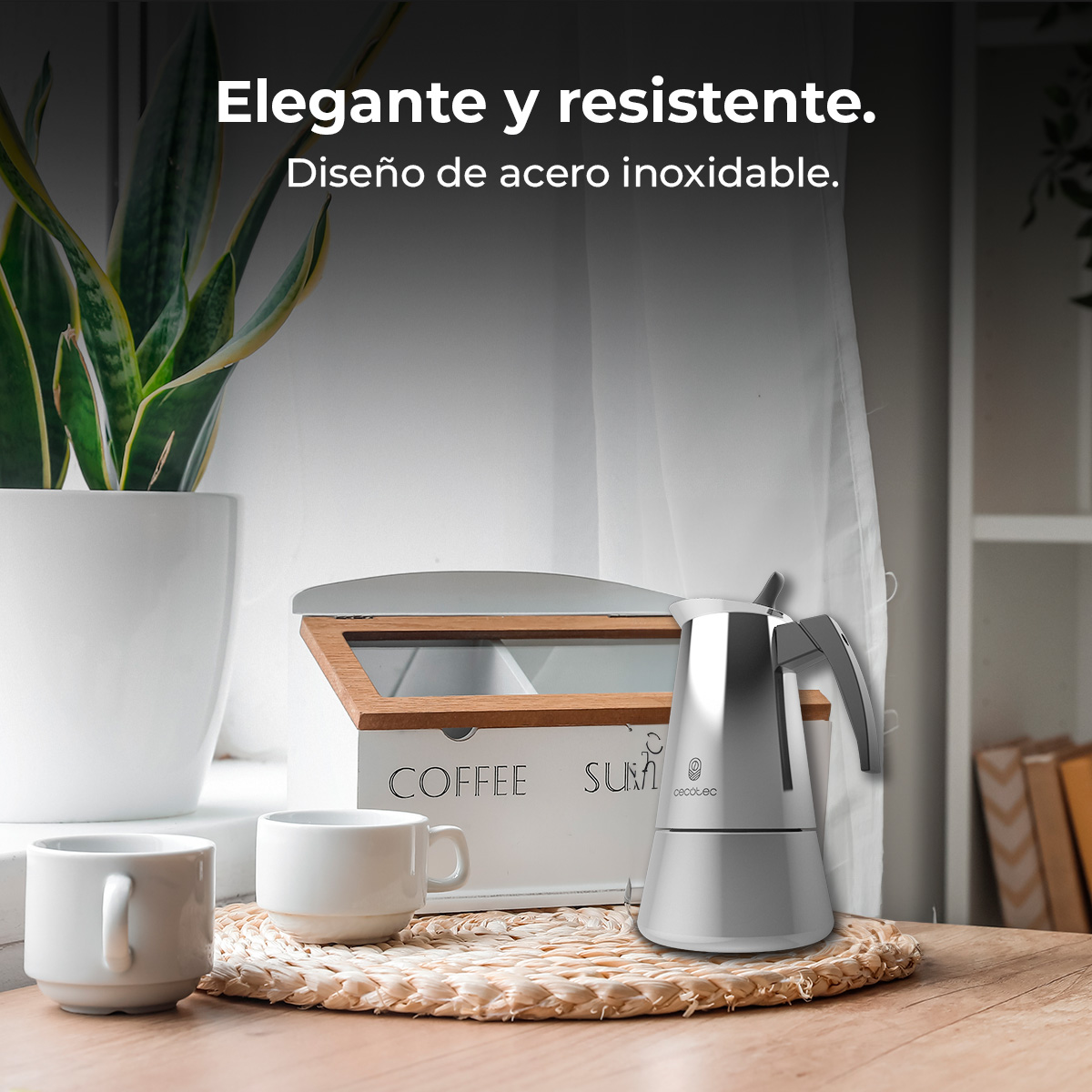 Una cafetera plateada, dos tazas y un bote de café sobre una mesa.