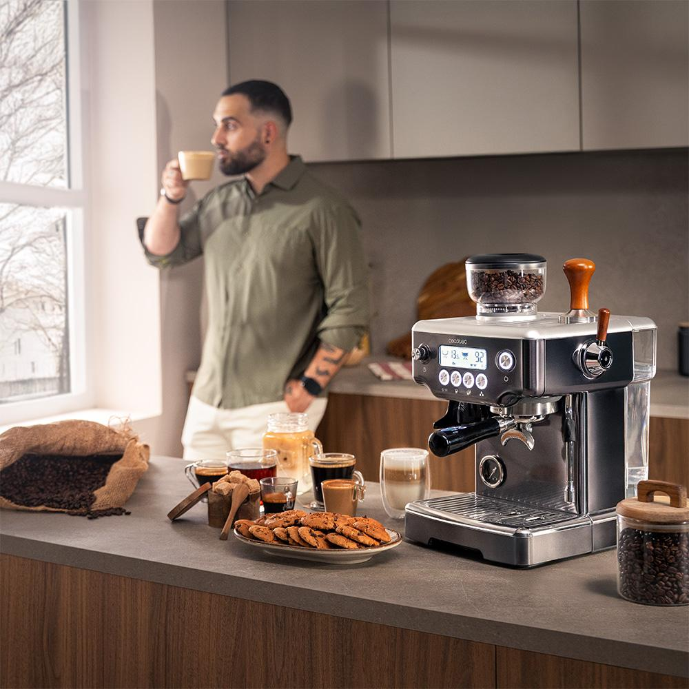 Hombre bebe café junto a una máquina de espresso con pasteles y granos de café.