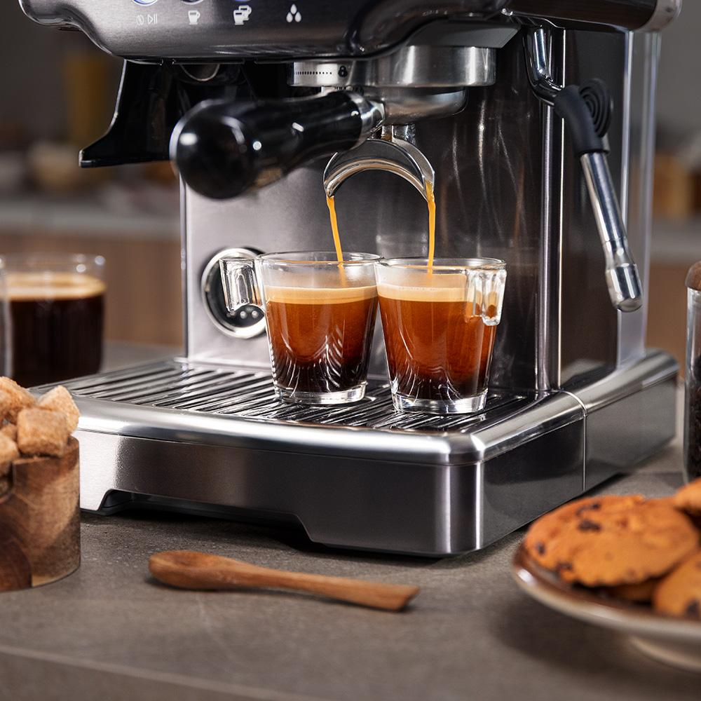 Máquina de espresso preparando dos tazas de espresso, con terrones de azúcar y galletas cerca.