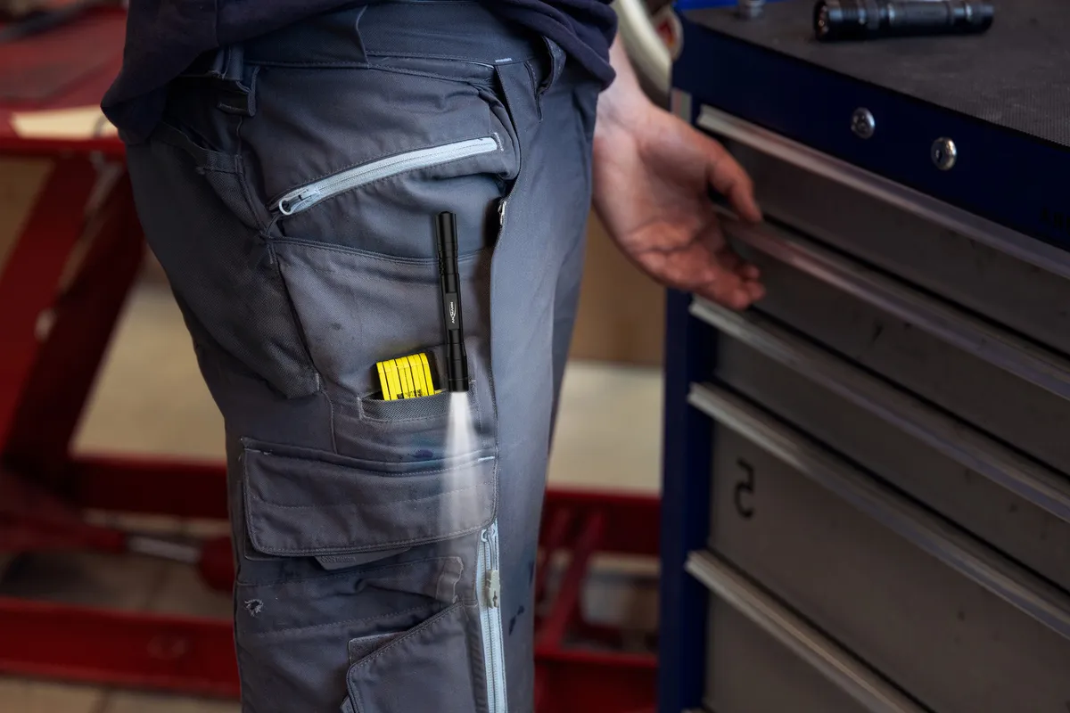 Un homme en pantalon de travail avec une lampe torche et un mètre dans la poche.