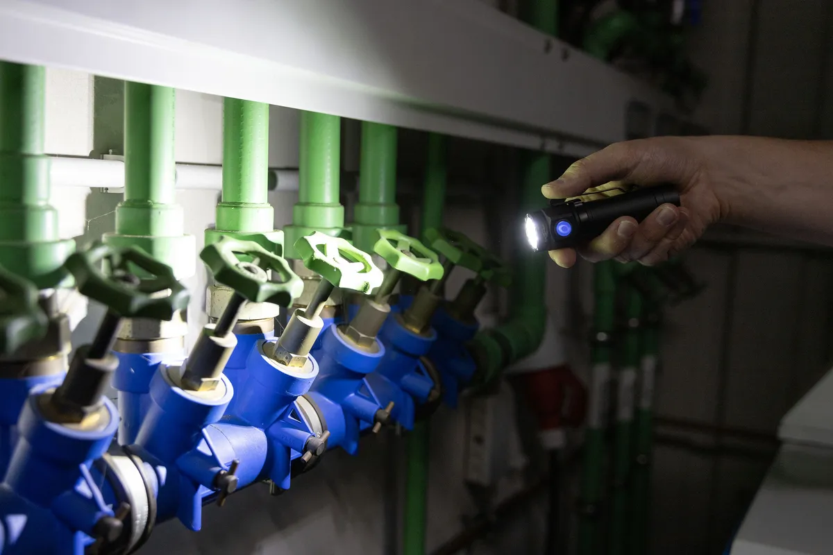 Main éclaire des vannes bleues et tuyaux verts avec lampe torche.