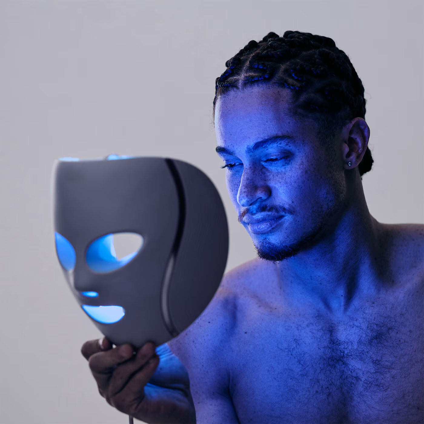 Un homme tient un masque facial lumineux. Des lumières bleues l'illuminent.