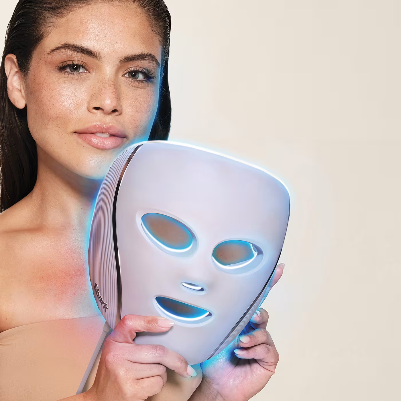 Une femme tient un masque LED blanc avec des lumières bleues devant son visage.