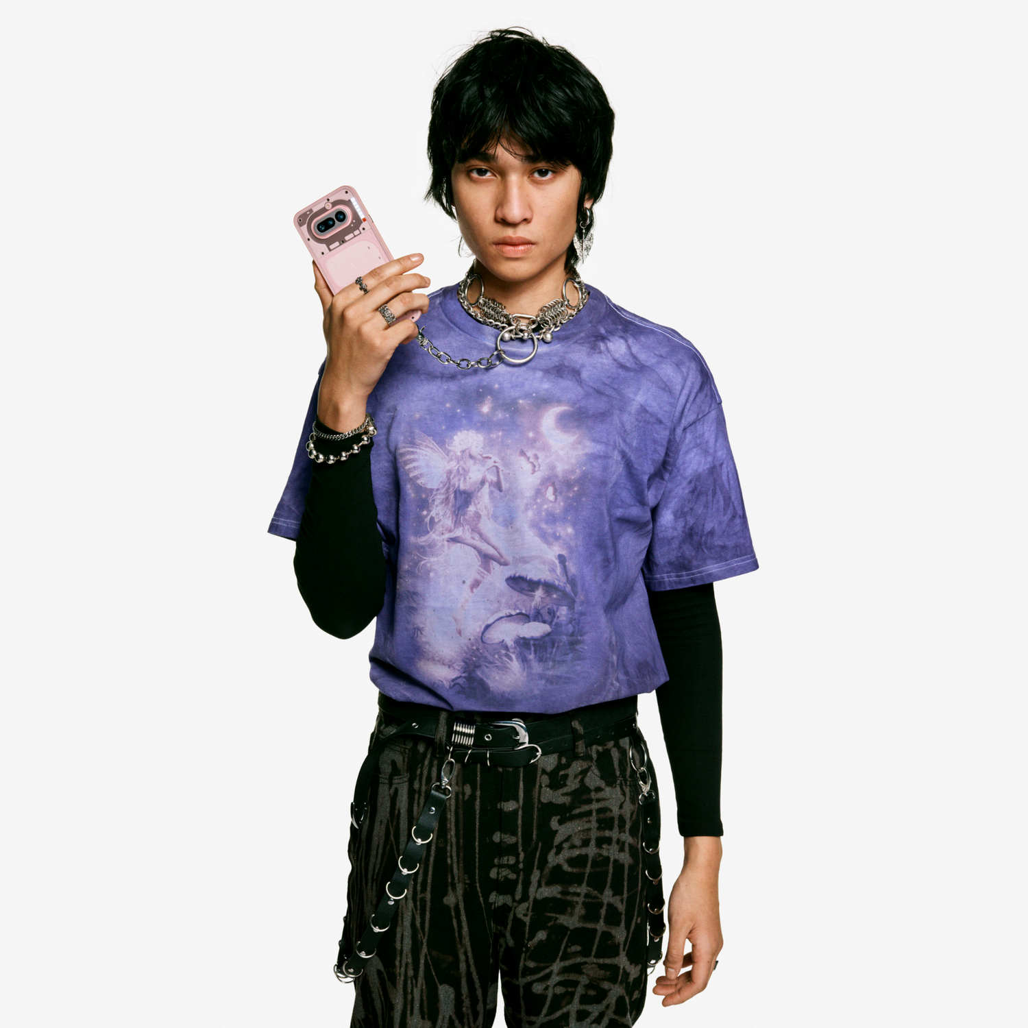 Una persona con pelo oscuro sostiene un teléfono rosa. Viste una camiseta morada.