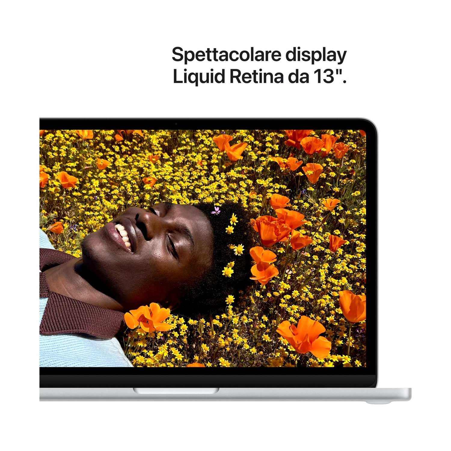 Uomo sdraiato in un campo di fiori gialli e arancioni, mostra un MacBook.