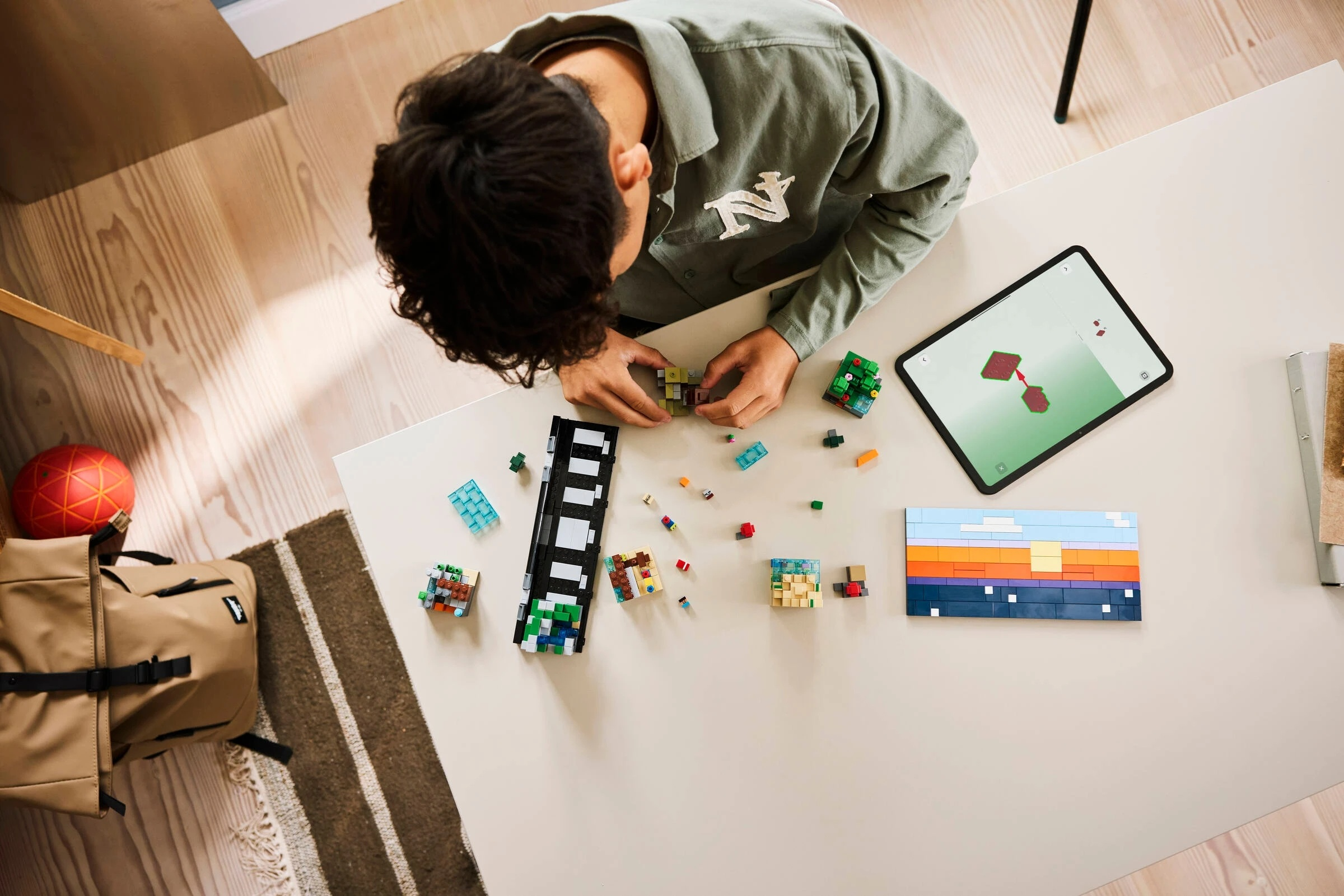 Osoba budująca kolorowe klocki Lego; tablet pokazuje instrukcje; mozaika Lego zachód słońca.